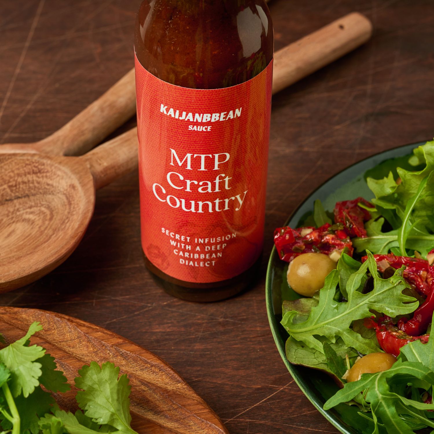 Bottle of Kailijnbbean MTP Craft Country sauce on a wooden surface with a salad.