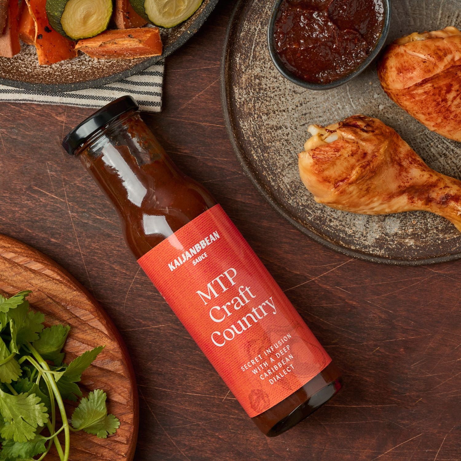 Bottle of MTP Craft Country hot sauce on a wooden surface with food items around